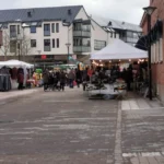 Marknadsstånd och besökare på Falköpings Höstmarknad. Täckt marknadsgata med kläder, hantverk och försäljning på Stora torget en kylig höstdag.