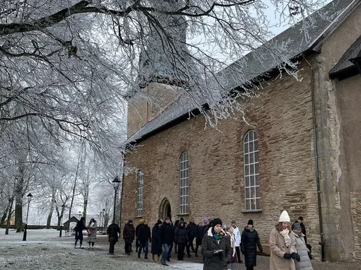 S:t Olof Kyrkan och vinterstämning med FalbygdsTurism En grupp människor utanför S:t Olof Kyrkan under vintriga förhållanden. Snö täcker marken och träden för en stämningsfull upplevelse.
