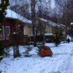 Snötäckta hus och granrisdekorationer längs hantverksbyns gata, upplysta av julbelysning.
