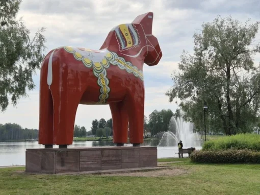 Näst största dalahästen i världen står vid vattnet i Mora, med fontän och träd i bakgrunden.