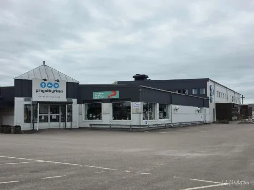 Pingstkyrkan Second Hand i Falköping med stor butiksbyggnad, entré och parkeringsyta utanför.