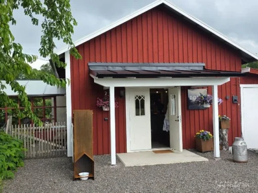Torp1 i Östra Tunhem med röd träfasad, entré, blommor och liten butik på vägen mot Mösseberg.