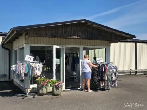 Kinnarps Presentshop i Kinnarp med klädställningar utanför entrén, blommor vid dörren och besökare som tittar på kläder.